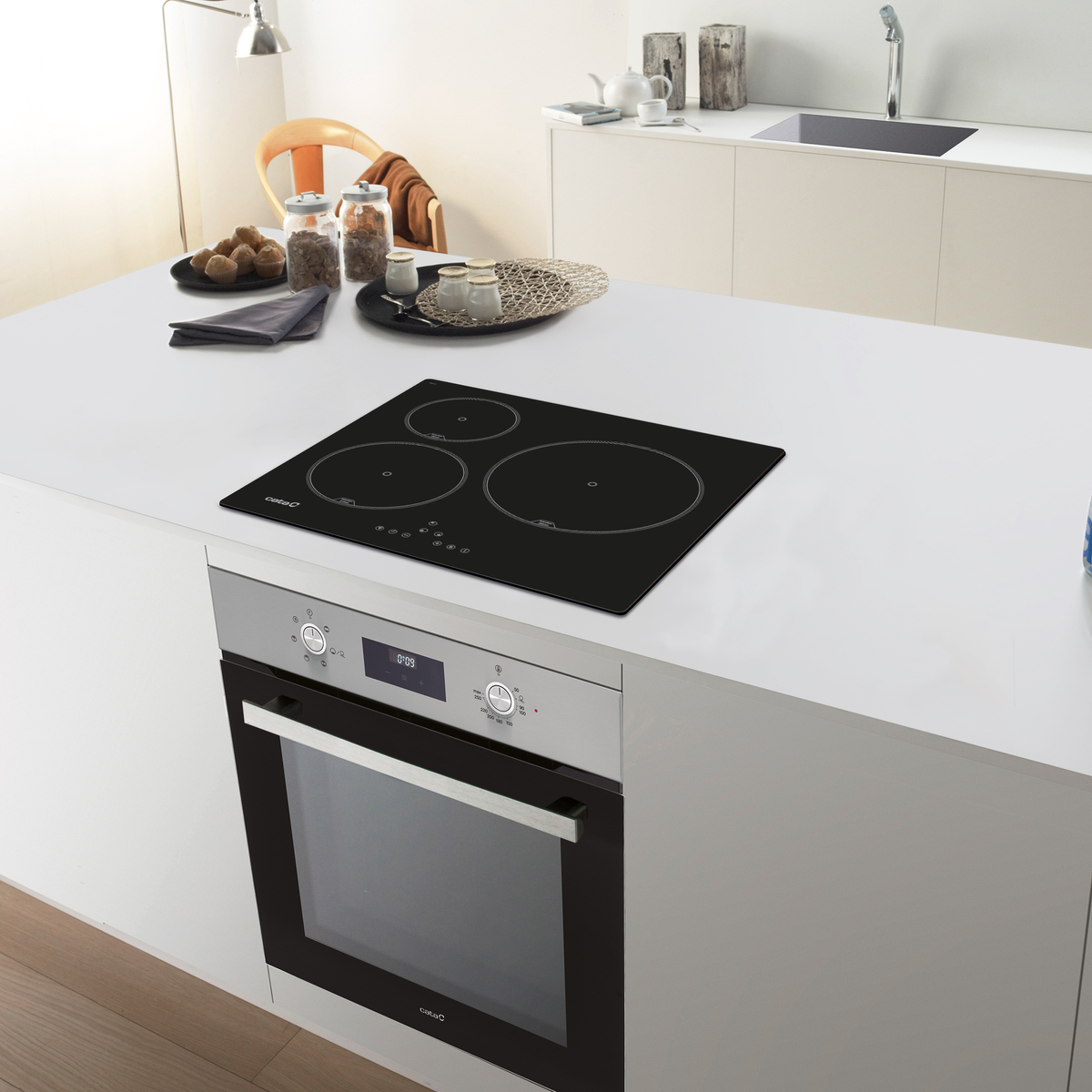Isla de cocina moderna con placa de cocina negra y horno. La escena incluye una encimera blanca y otros elementos de cocina.