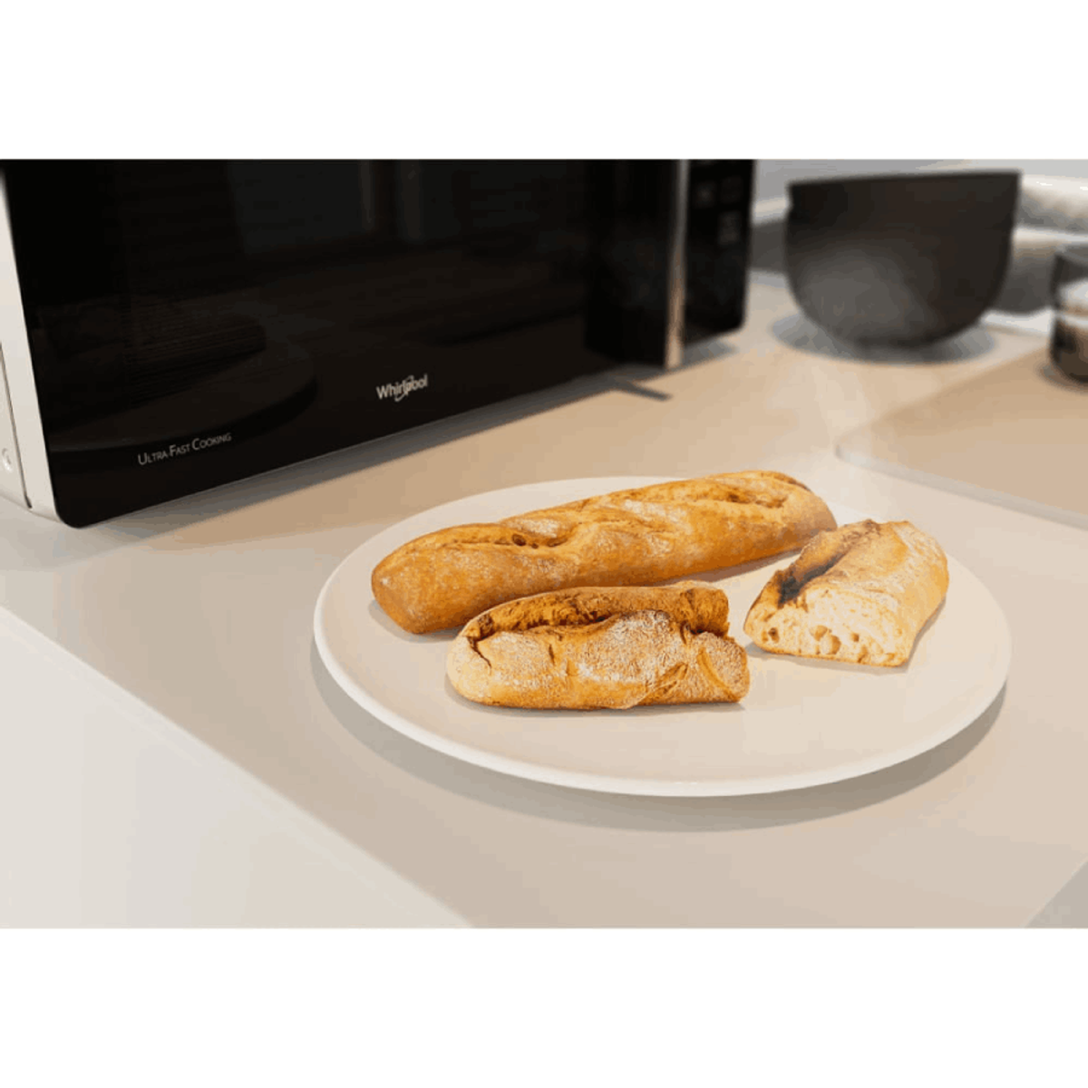 Un piatto bianco con tre pezzi di pane davanti a un forno a microonde.