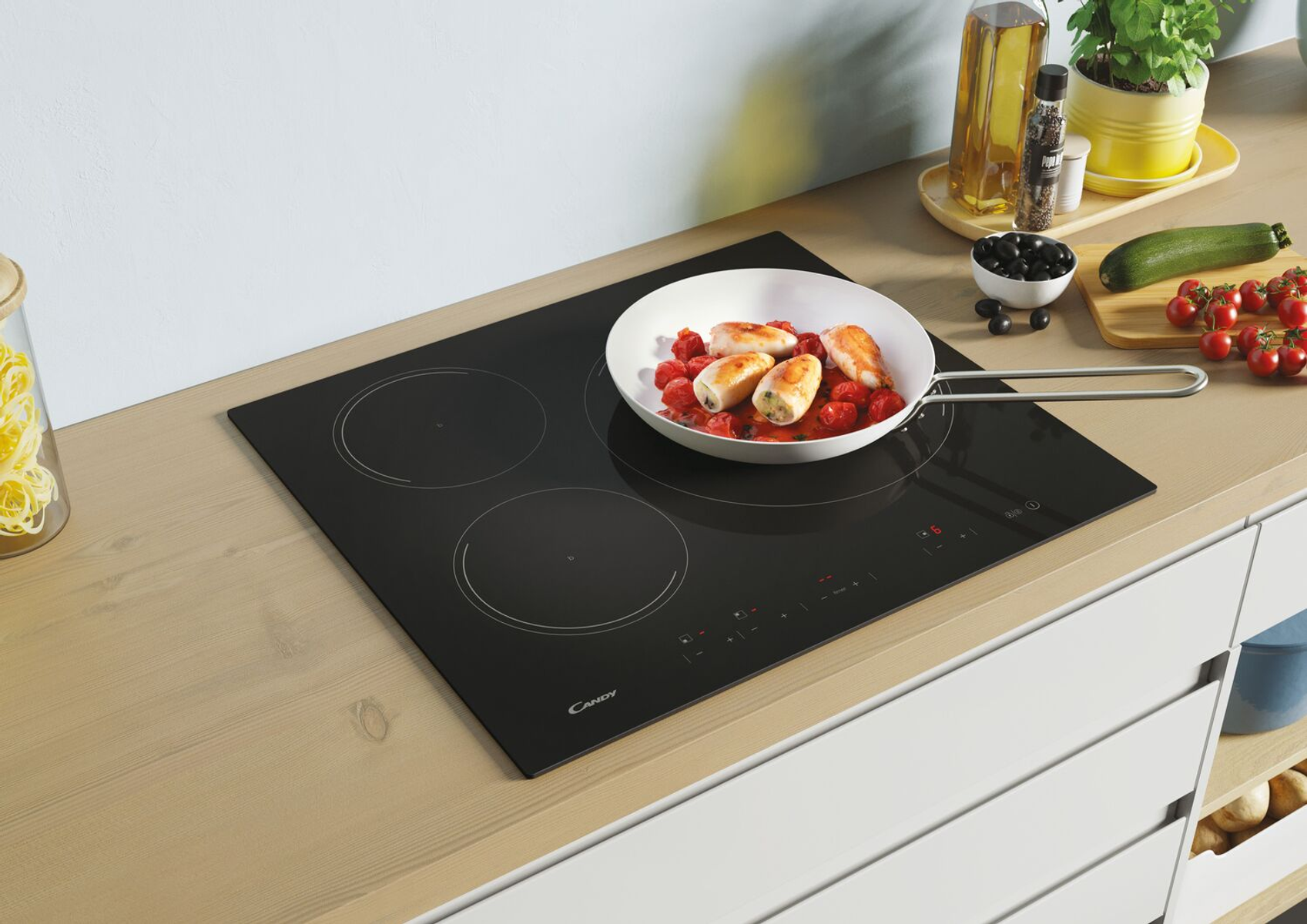 Czarna płyta grzewcza z 3 okręgami i jedzeniem na patelni. Drewniany stół i białe szafki w tle.