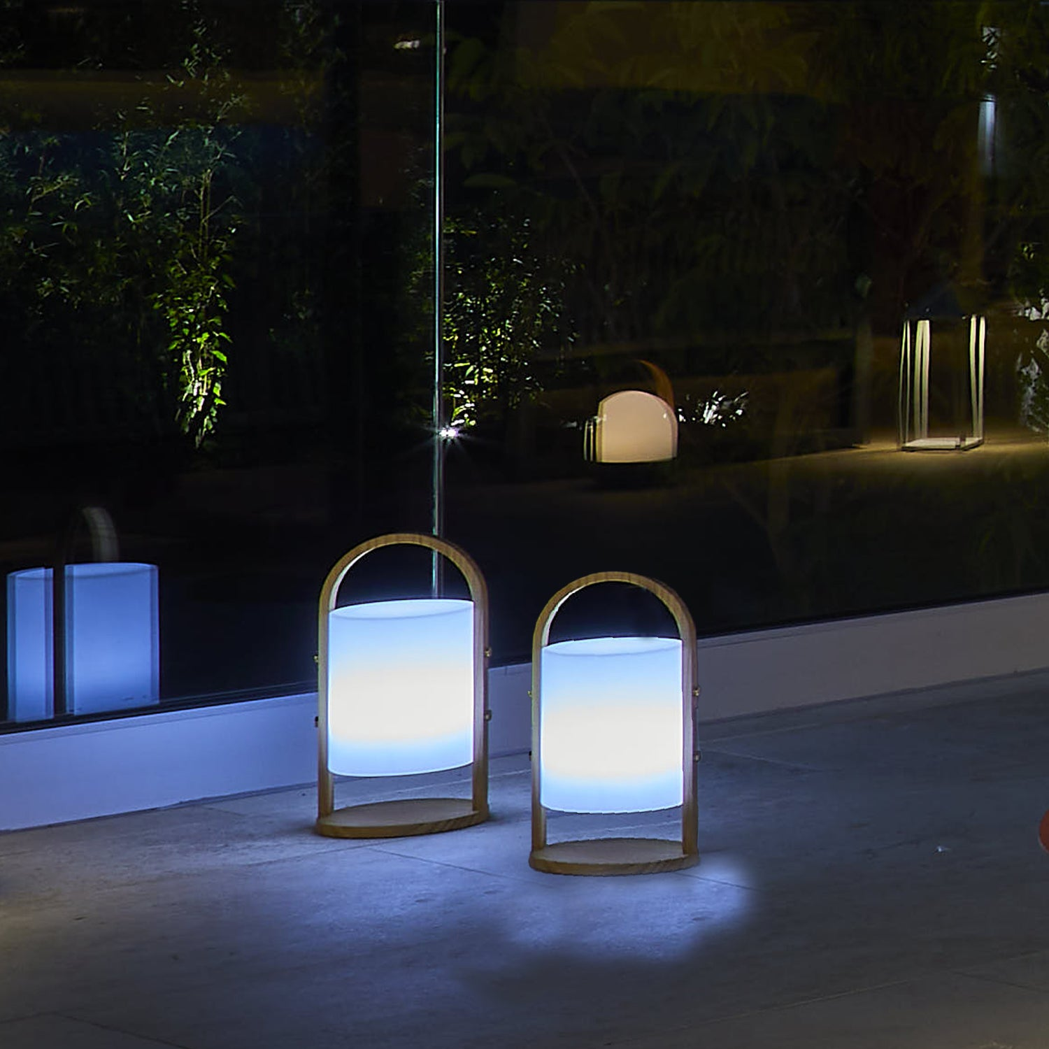 Zwei Außenlampen mit Holzbogen, nachts blau und weiß leuchtend.