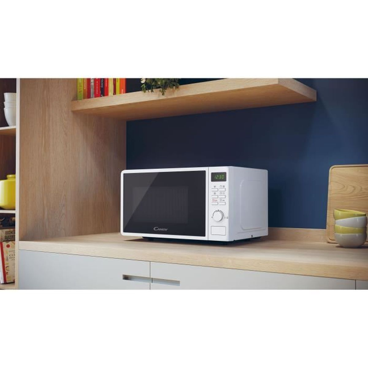 Biała kuchenka mikrofalowa stoi na białym i drewnianym blacie. Za nią znajduje się granatowa ściana.