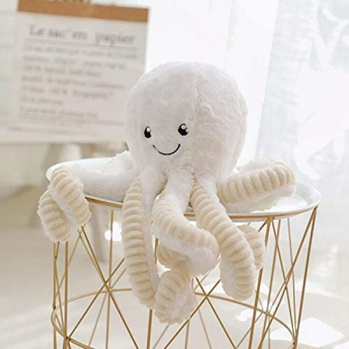 Ein weißes Plüsch-Oktopus-Spielzeug mit lächelndem Gesicht, das auf einem goldenen Drahtständer sitzt.