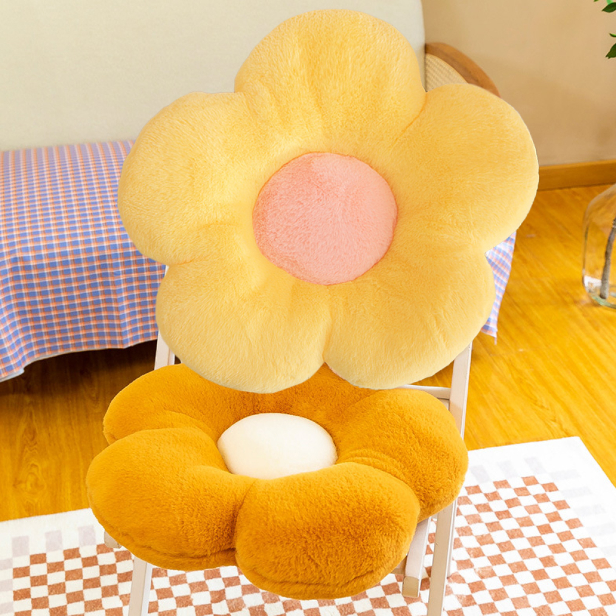 Zwei blumenförmige Kissen auf einem Stuhl. Das obere ist gelb, das untere orange. Hintergrund ist ein Raum.