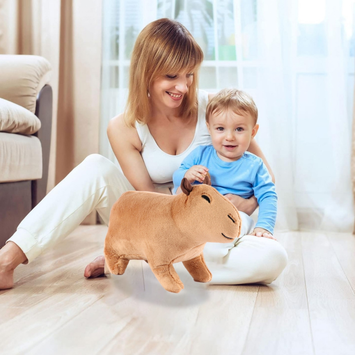 Frau mit Baby, das ein braunes Capybara-Plüschtier auf einem Holzboden hält. Beide lächeln.