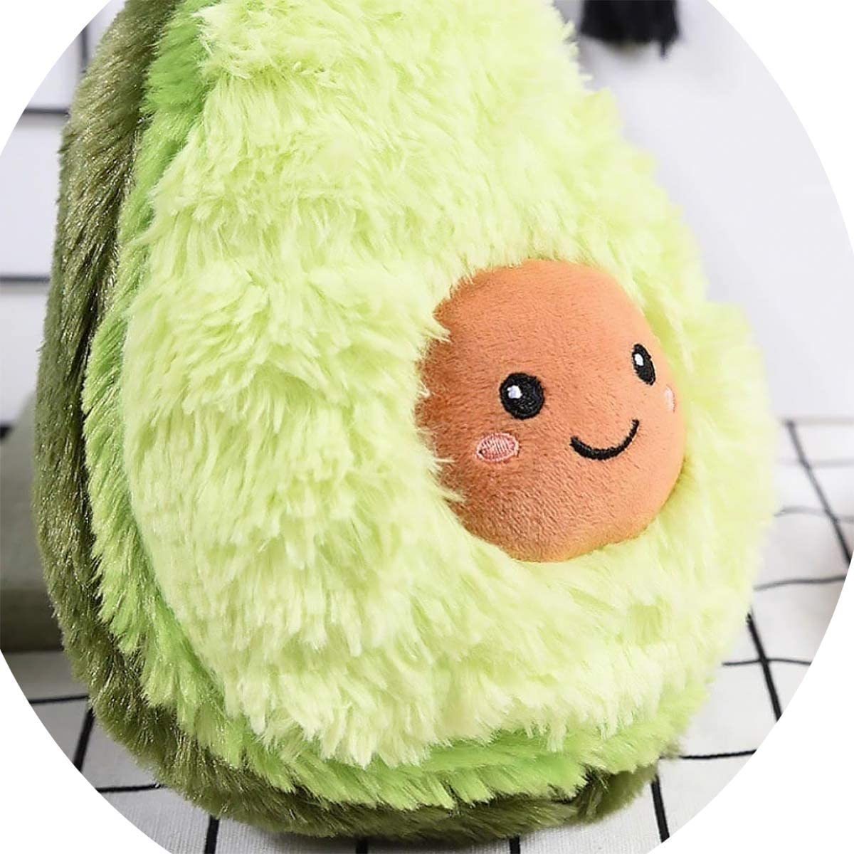 Plüschtier einer Avocado, außen grün mit einem lächelnden Gesicht innen, auf karierter Oberfläche.