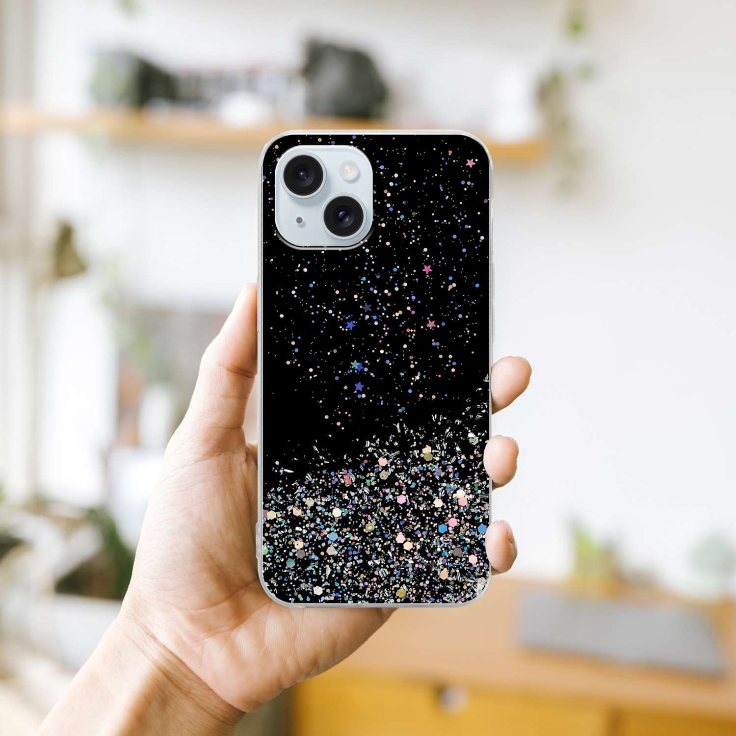 Una mano sosteniendo una funda de teléfono negra con un diseño de purpurina. La funda tiene un recorte para la cámara.