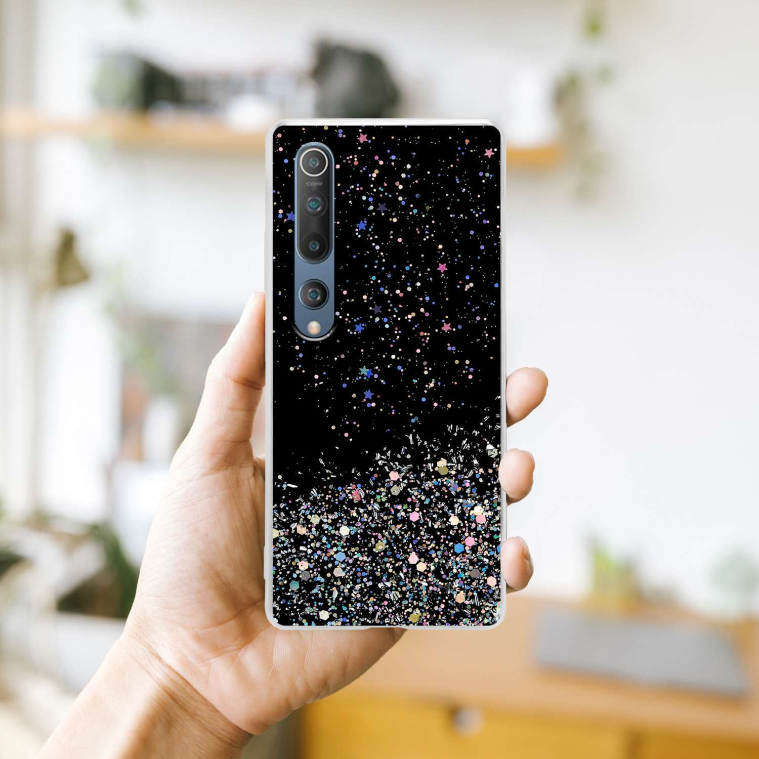 Una mano che tiene una custodia con glitter e stelle su sfondo nero, mostrando le fotocamere del telefono.