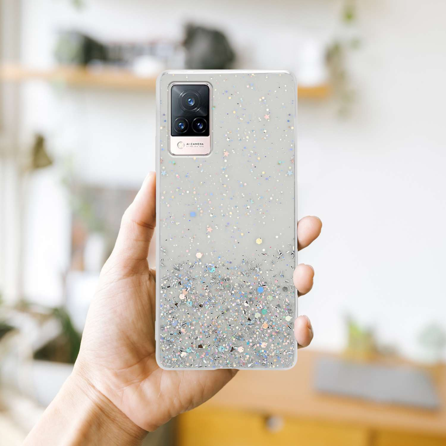 Mano che tiene un telefono con custodia glitterata. Sfondo sfocato.