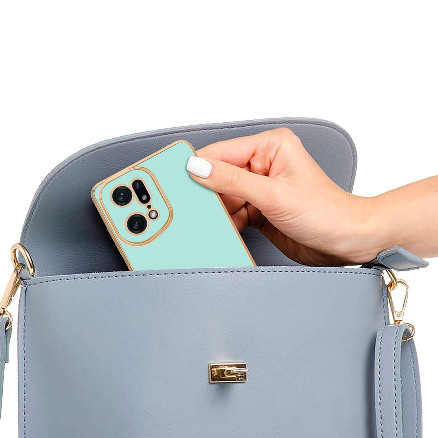 Una mano tiene un telefono verde menta all'interno di una borsa grigia. Il telefono ha una cornice dorata per la fotocamera.