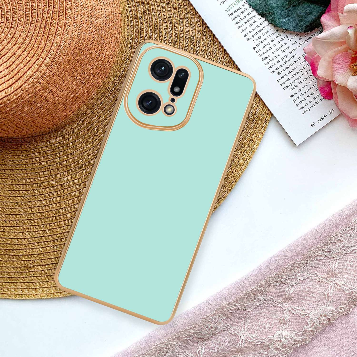 Custodia per telefono verde menta con finiture dorate su una scrivania accanto a un cappello e una sciarpa.