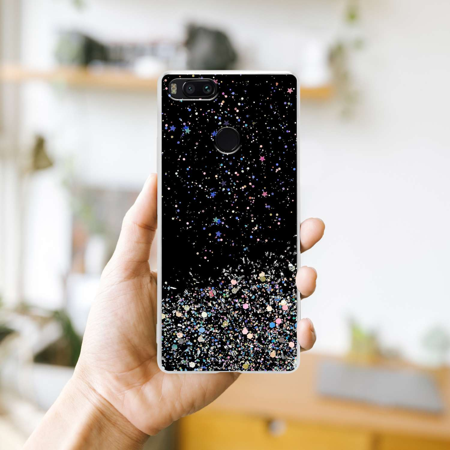 Mano che tiene un telefono con un design nero glitterato, con macchie colorate. Sfondo sfocato.