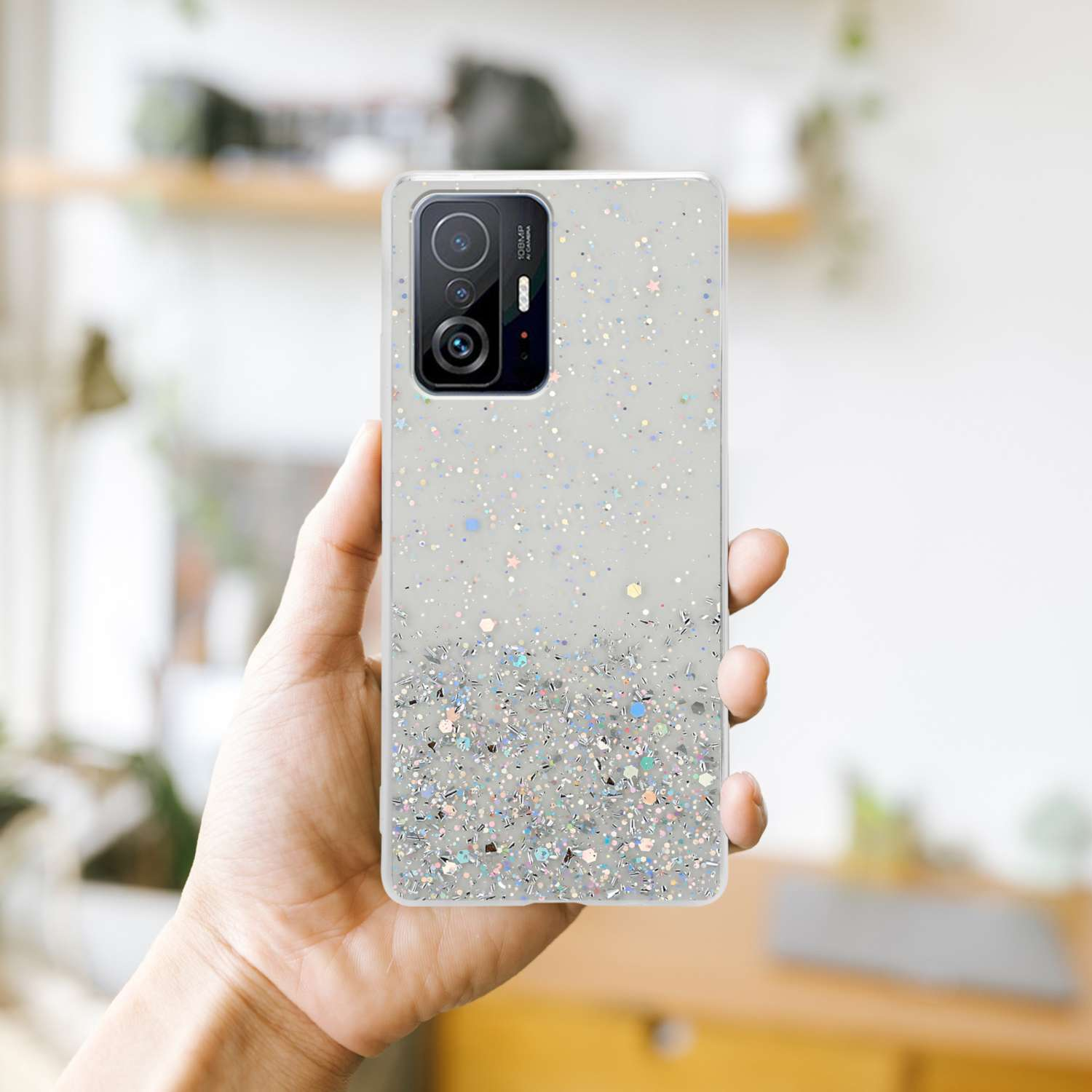 Una mano che tiene una custodia trasparente con glitter e stelle su uno sfondo sfocato.