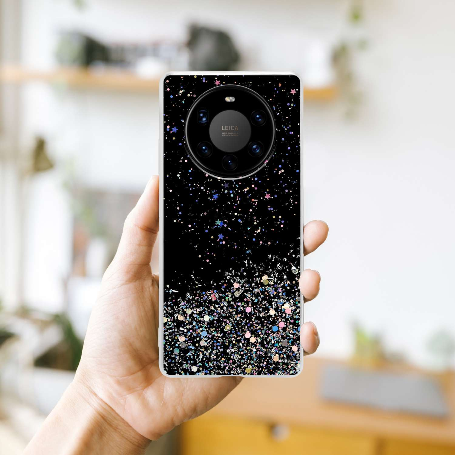 Mano che tiene custodia nera con design glitter, sfondo sfocato di una stanza.