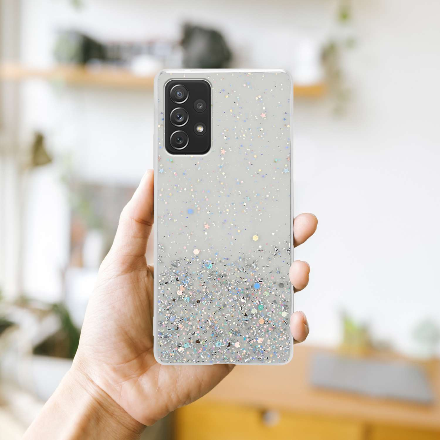 Mano che tiene una custodia per telefono con design glitterato. Sfondo sfocato.