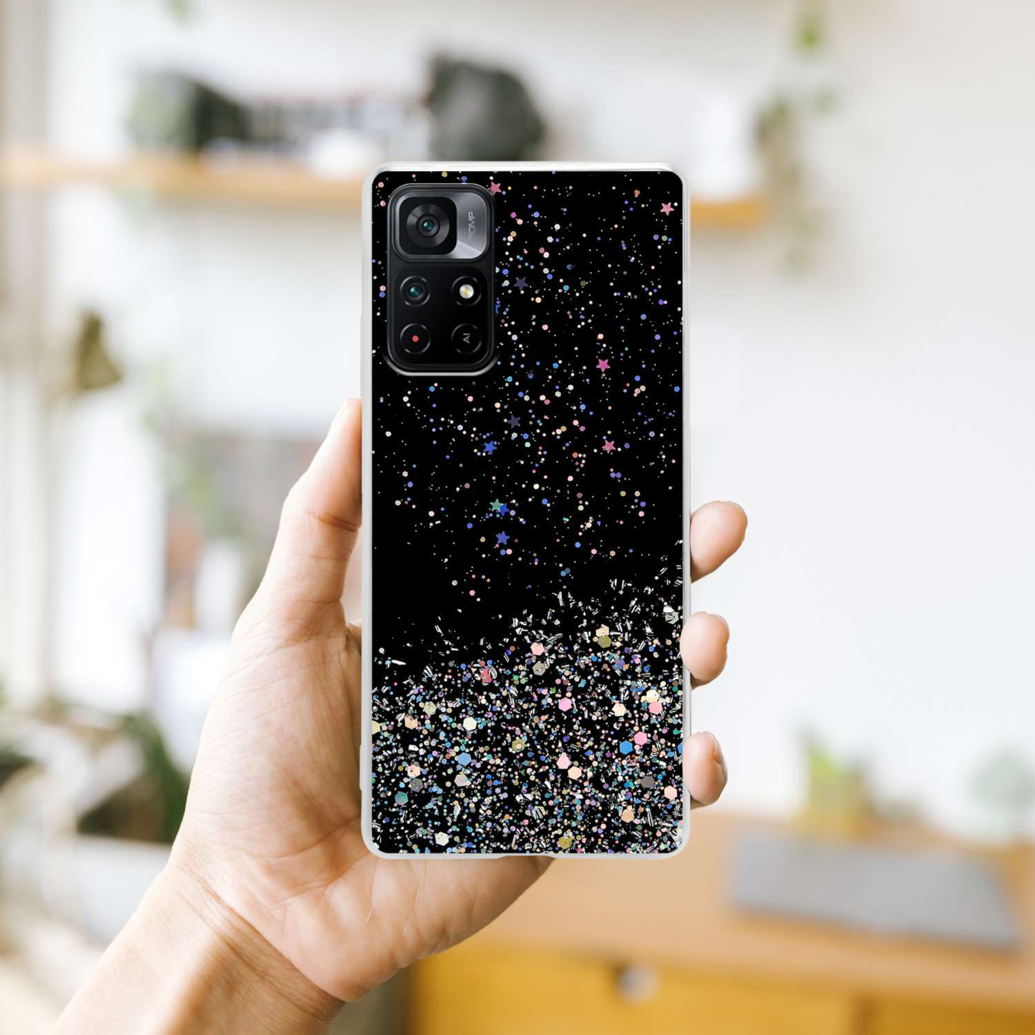 Una custodia per telefono nera tenuta in mano, ricoperta di glitter e stelle colorate. È visibile una fotocamera del telefono.
