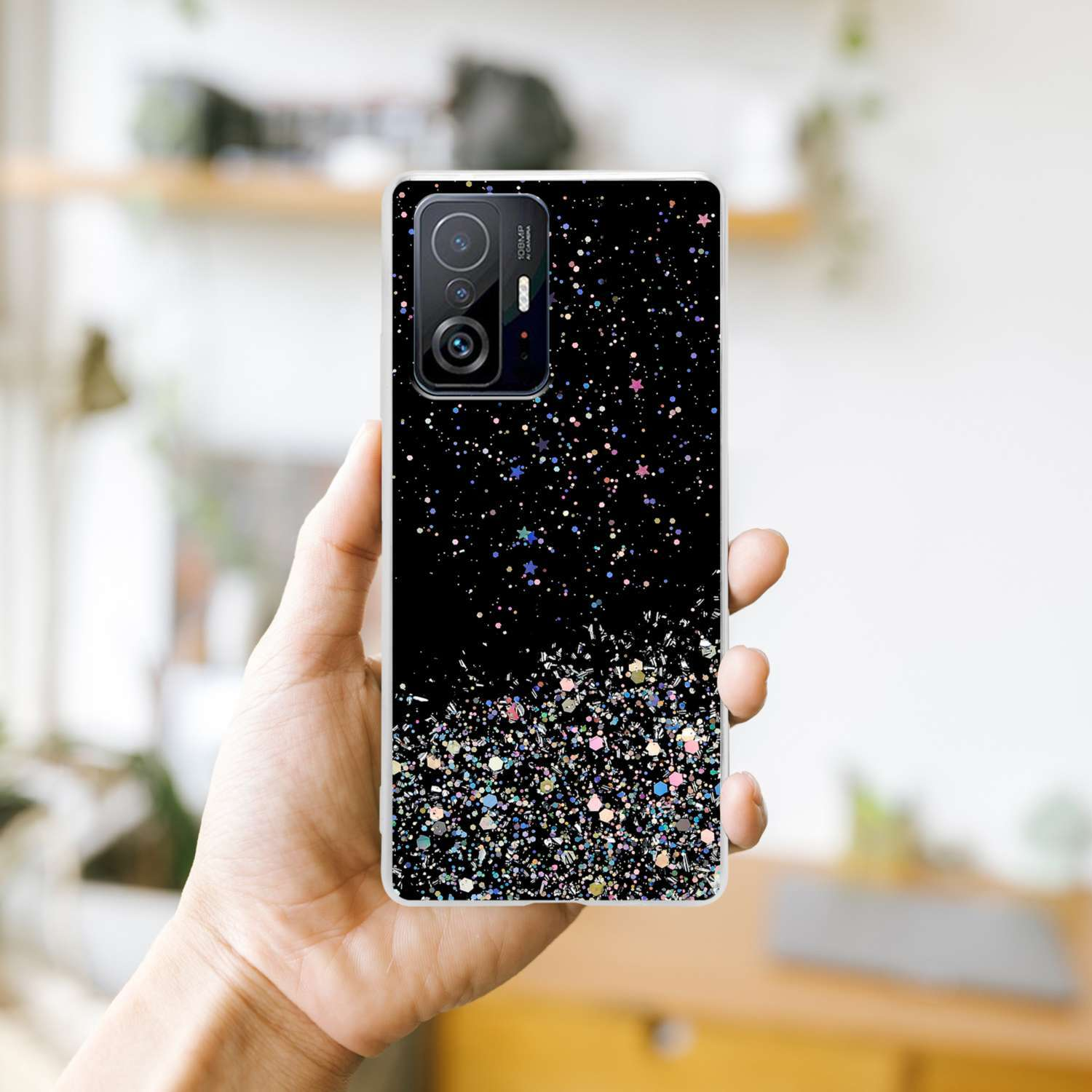 Mano che tiene un telefono con custodia nera glitterata. Sfondo sfocato.