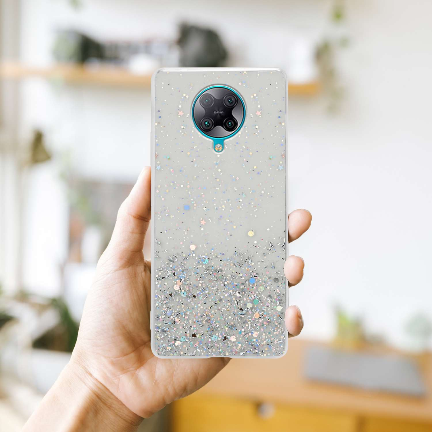 Una mano che tiene un telefono con una custodia scintillante. La custodia è coperta di glitter argentati.