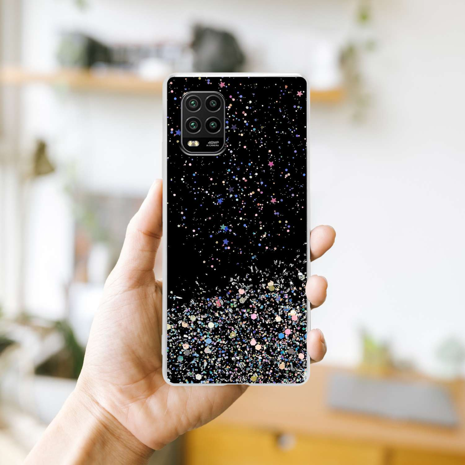 Una mano che tiene una custodia per telefono con un design glitter nero e scintille colorate su una superficie bianca.