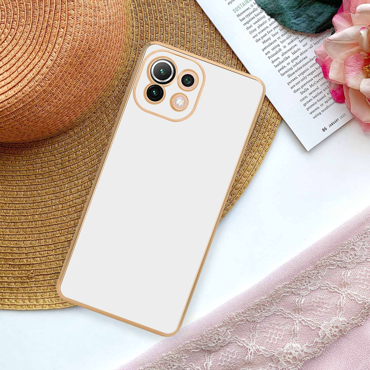 Telefono bianco con cornice dorata su un tavolo con rivista e tessuto rosa.