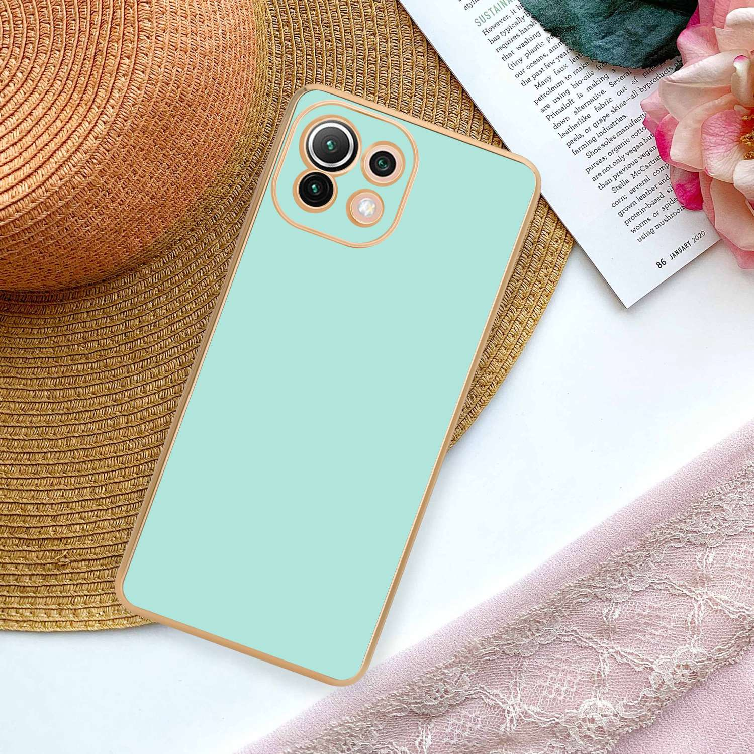Custodia per telefono verde menta con cornice dorata, posizionata accanto a un cappello e un panno rosa.