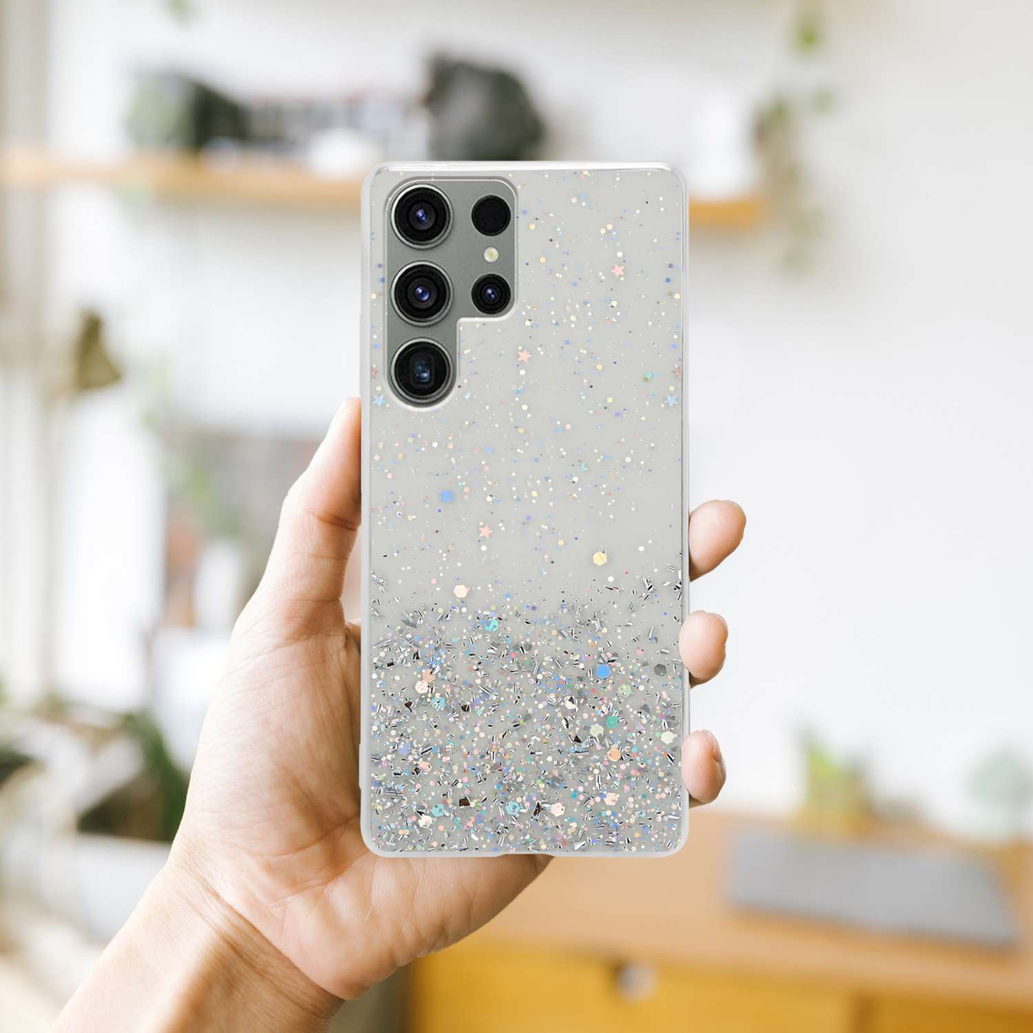 Hand, die ein Telefon mit glitzerndem Gehäuse hält. Der Hintergrund ist unscharf.