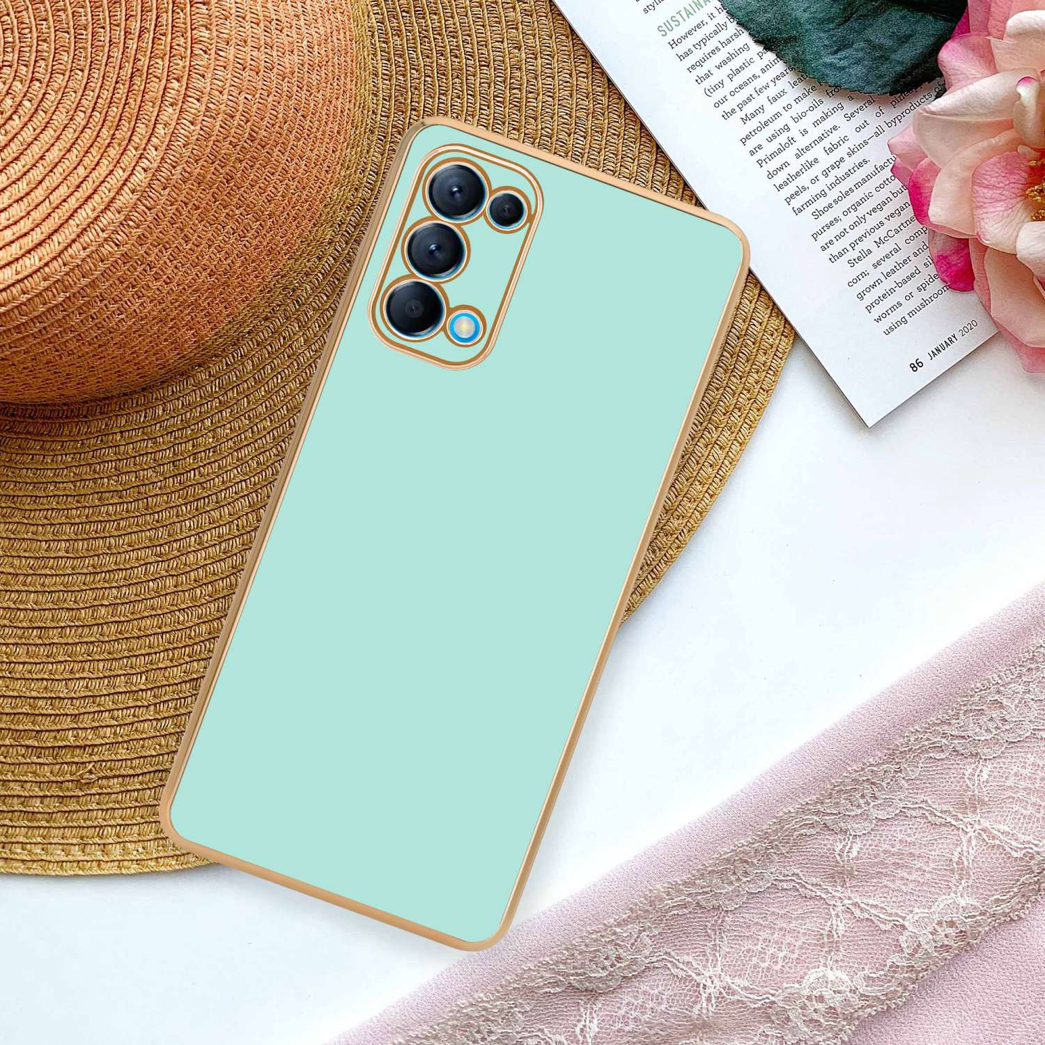 Una custodia per telefono verde chiaro su un cappello di paglia, con una sciarpa rosa e un foglio di carta con testo.