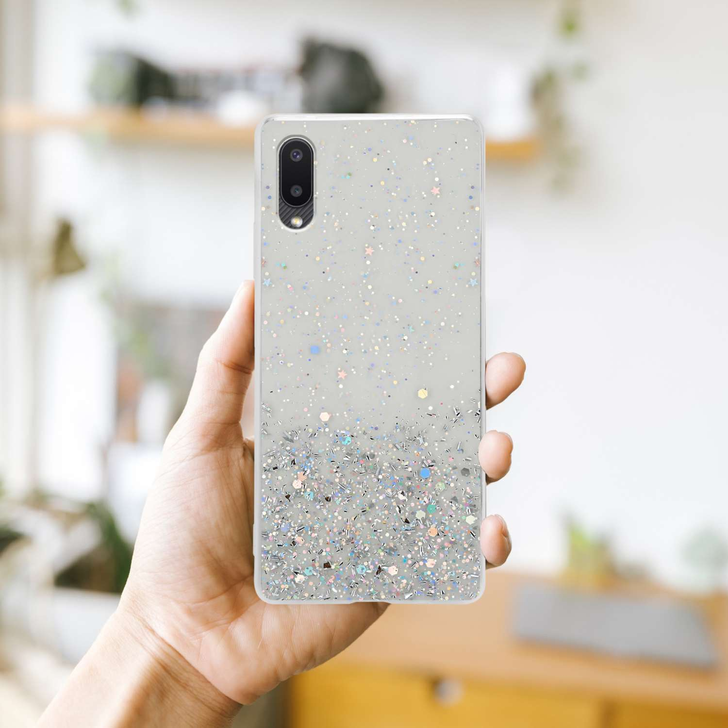 Mano che tiene un telefono con una custodia glitterata, con una sfumatura di glitter nella parte inferiore.