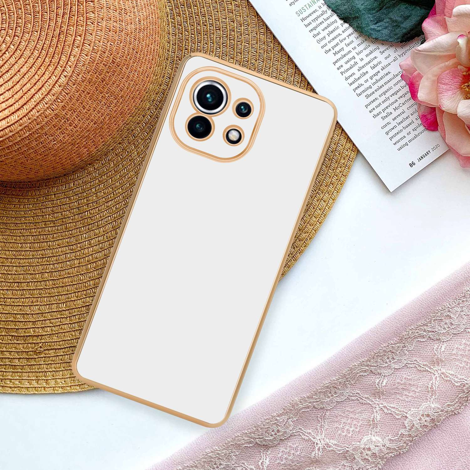 Custodia per telefono con retro bianco, sopra una rivista e un panno rosa. Cornice dorata.