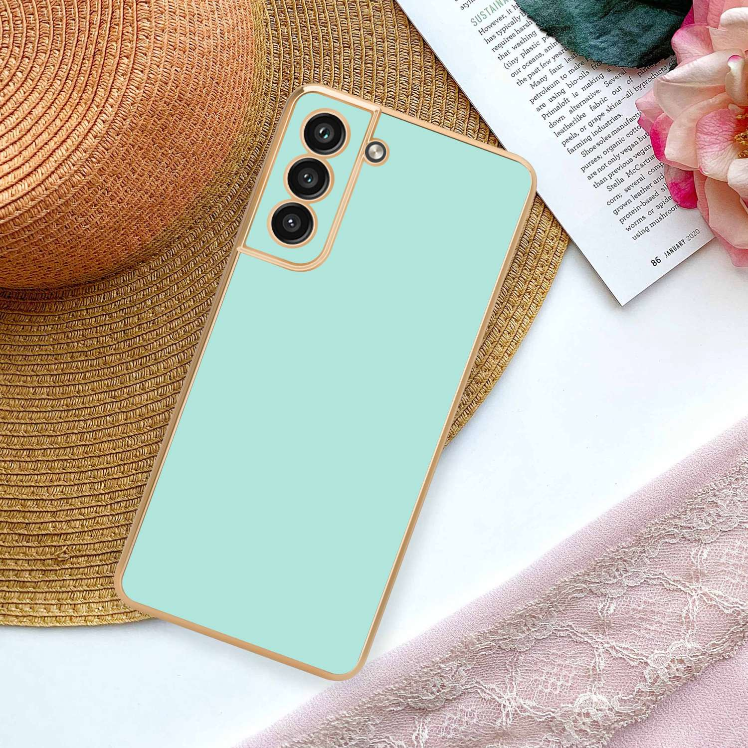 Una custodia per telefono verde chiaro su un cappello di paglia. C'è anche una sciarpa rosa e un foglio di carta con testo.