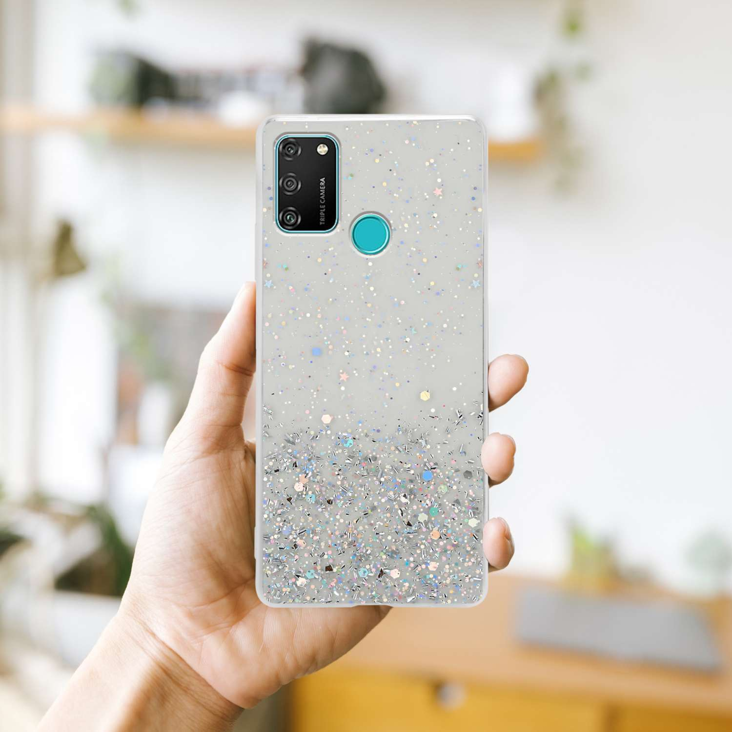 Hand hält ein Telefon mit glitzerndem Design. Das Telefon hat eine Dreifachkamera und eine türkisfarbene Taste.