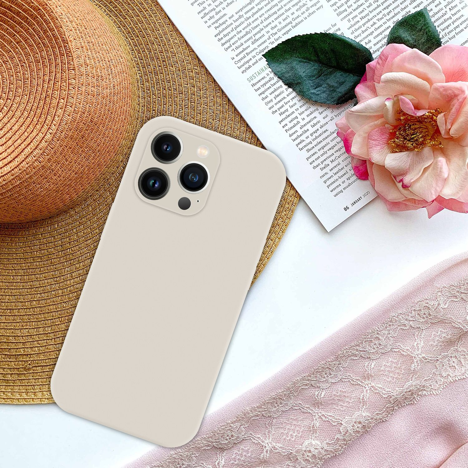 Beige Handyhülle mit drei Kameralinsen auf einem Tisch mit Hut und Blumen vor weißem Hintergrund.