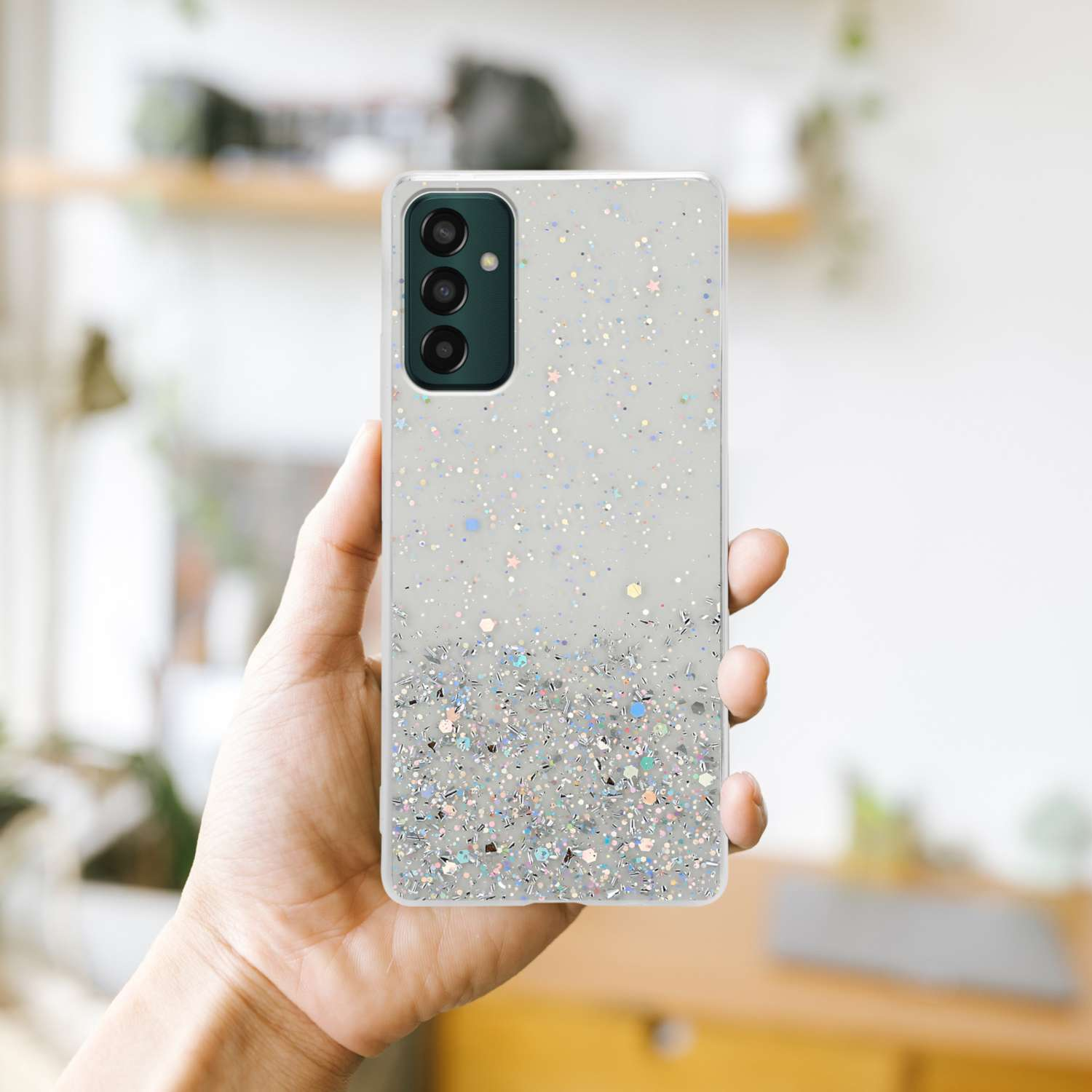 Una mano che tiene una custodia per telefono con glitter. La custodia è trasparente con glitter argentati e colorati.