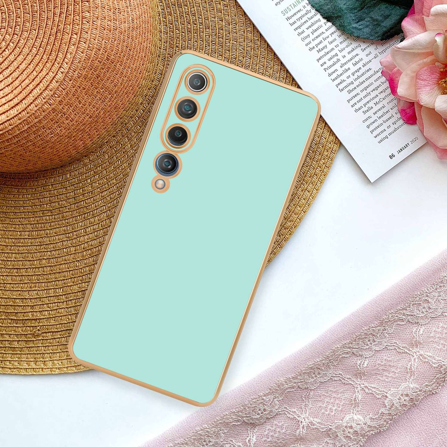 Una custodia per telefono verde menta con un telefono all'interno. È su un tavolo con un cappello e un panno rosa.