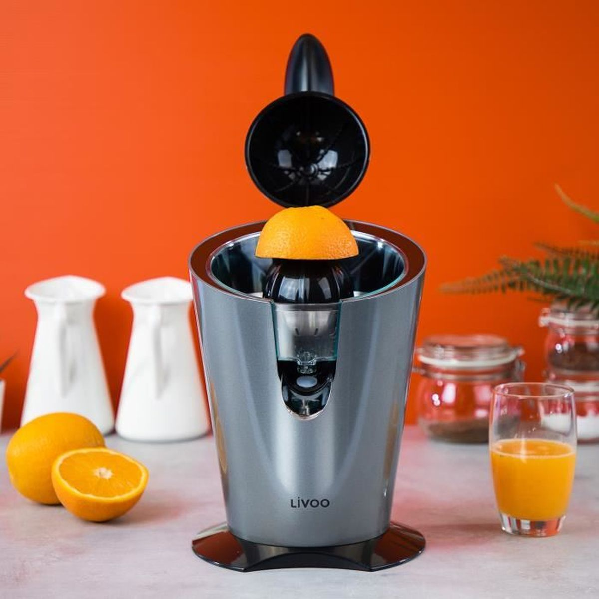 Entsafter mit Orangenhälfte, orangefarbener Hintergrund, Saft und weitere Objekte.