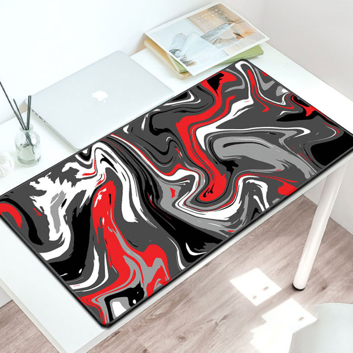 Mauspad mit einem schwarzen, roten und weißen abstrakten Design, auf einem weißen Schreibtisch. Laptop und Stifte sind sichtbar.