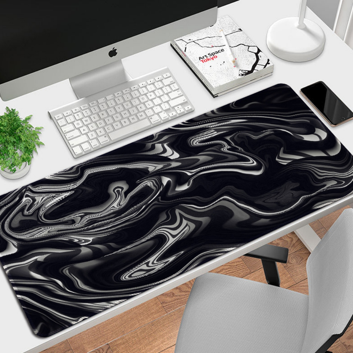 Schreibtisch mit Mauspad mit schwarz-weißem Marmordruck. Computer, Tastatur und Pflanze stehen auf dem Schreibtisch.
