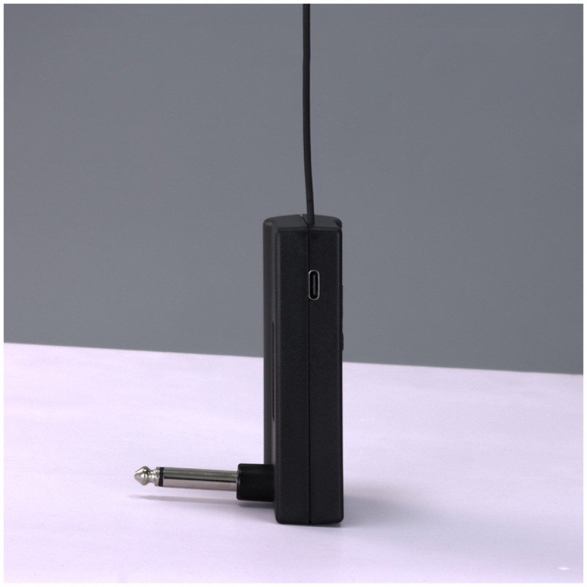 Czarny odbiornik audio ze srebrną wtyczką i czarnym przewodem. Tło jest białe i szare.