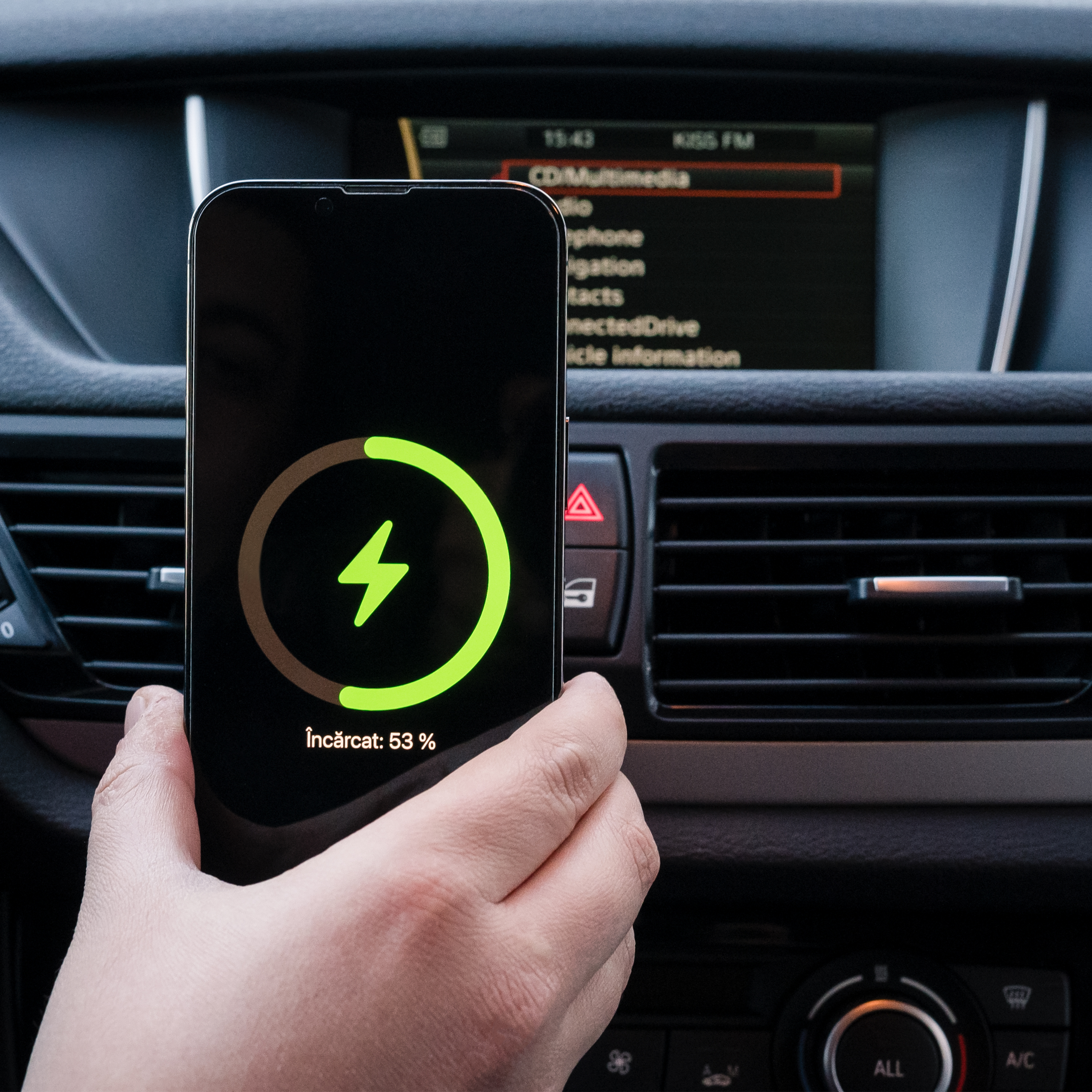 Ręka trzyma telefon ładujący się w samochodzie. Ikona ładowania na ekranie.