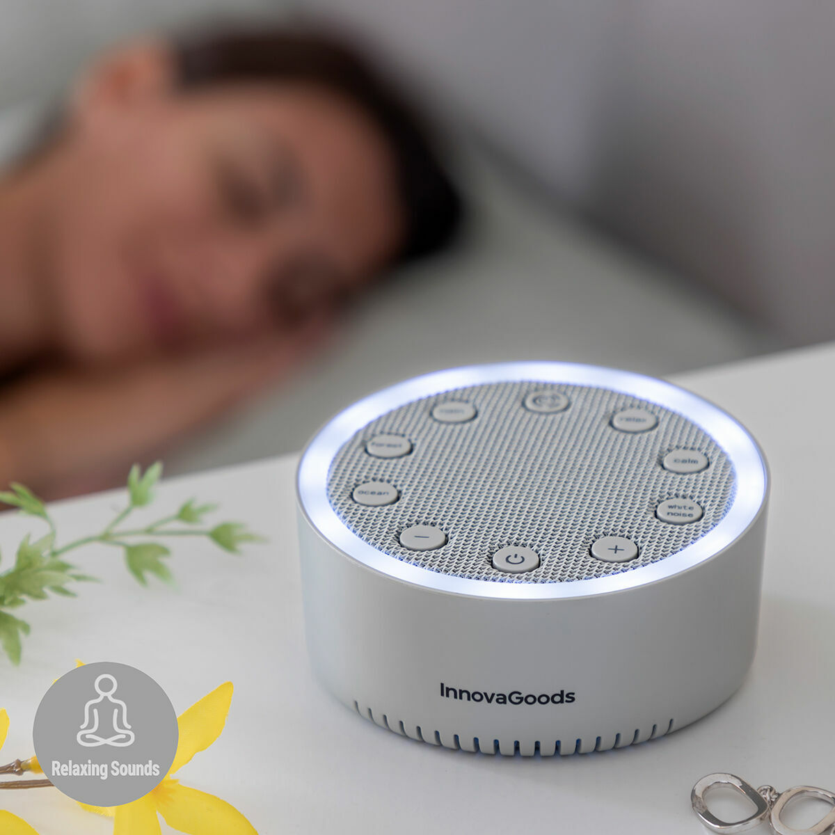 Una máquina de sonido blanca con botones. Una mujer está durmiendo en el fondo. Hay anillos.