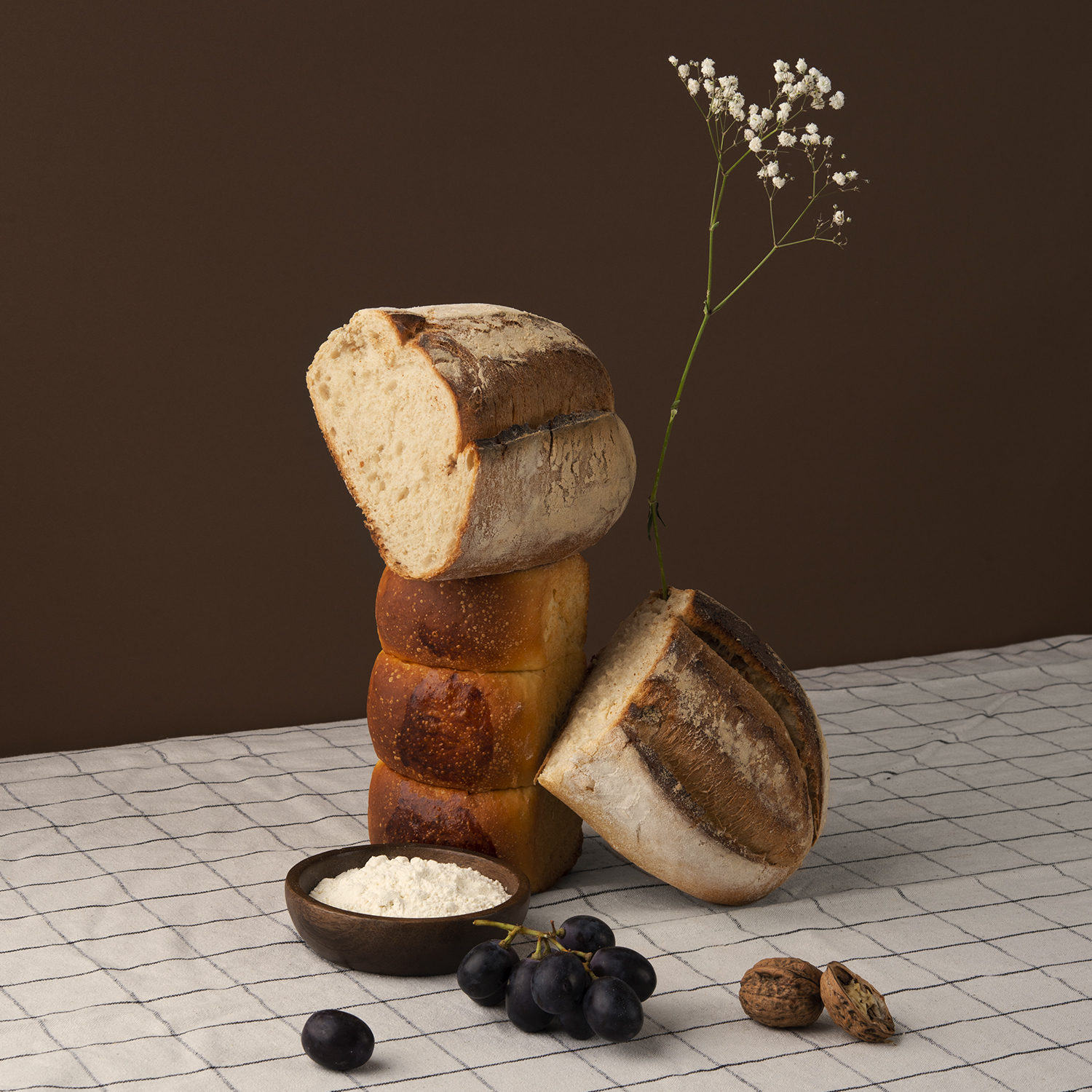 Composizione di pane: pagnotta a fette, pagnotte impilate, farina, uva e noci.