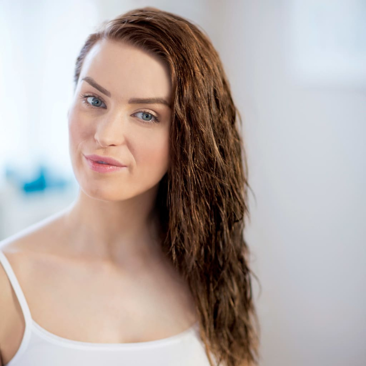 Kobieta z mokrymi włosami, patrząca w kamerę, ubrana w biały top.