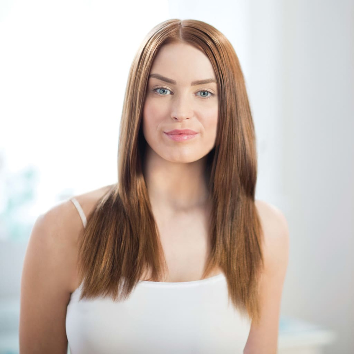 Kobieta z długimi, prostymi brązowymi włosami i białym topem uśmiecha się do kamery.
