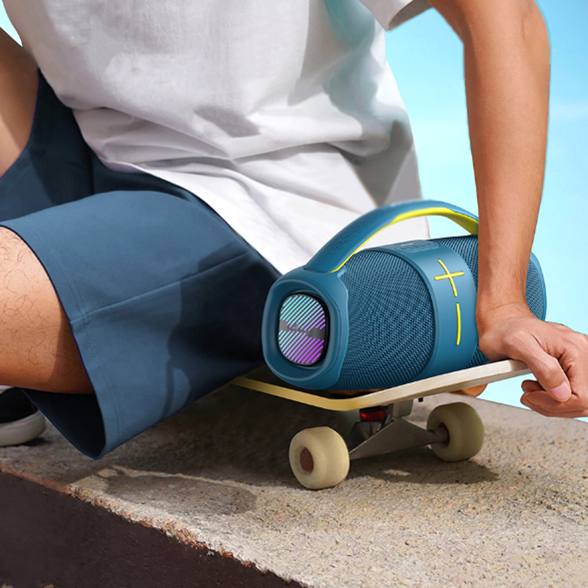 Eine Person hält einen blau-schwarzen Lautsprecher auf einem Skateboard vor blauem Hintergrund.