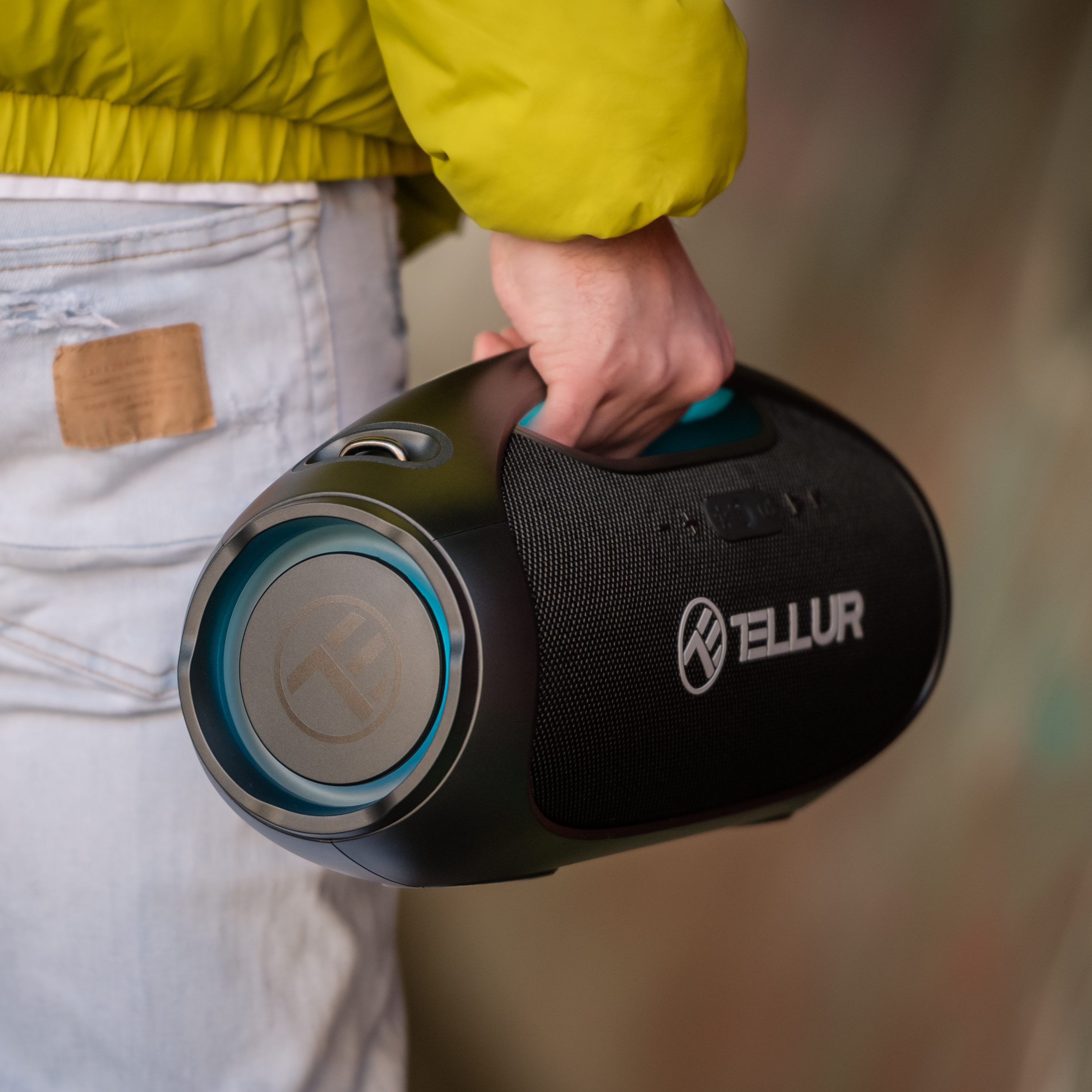 Osoba trzymająca czarnego boomboxa z niebieskim głośnikiem. Na boomboxie napis TELLUR.