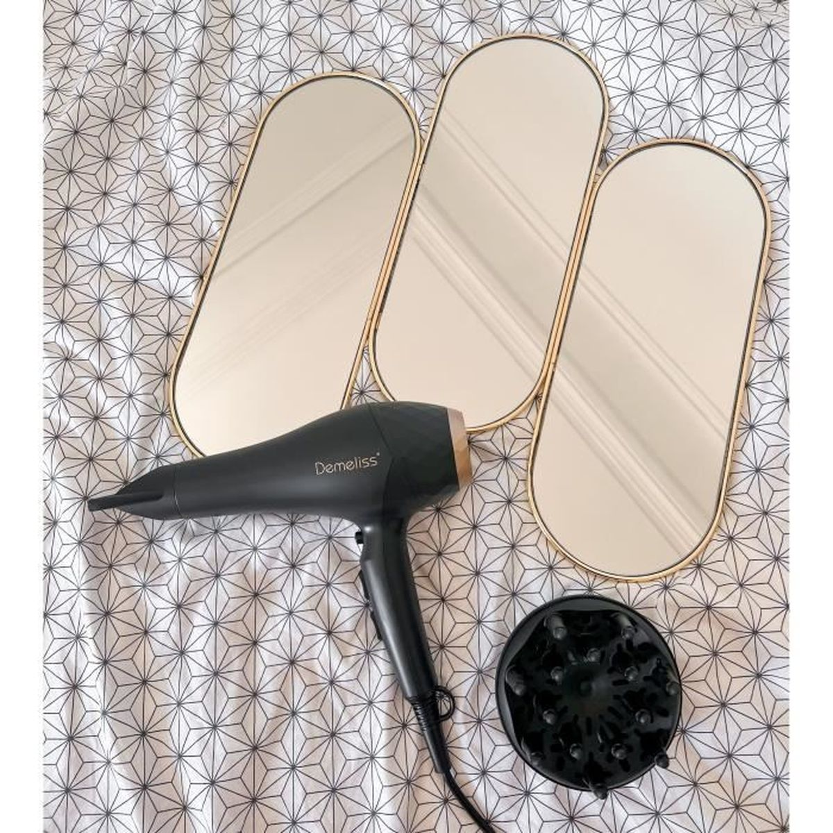 Trzy lustra z suszarką i dyfuzorem na wzorzystym prześcieradle.