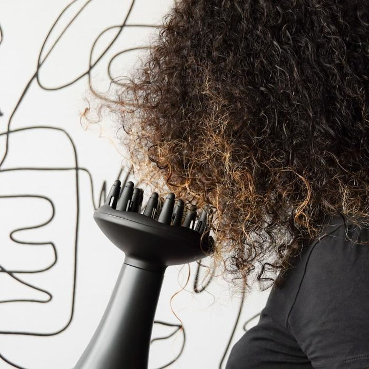 Osoba suszy kręcone włosy czarną suszarką do włosów.