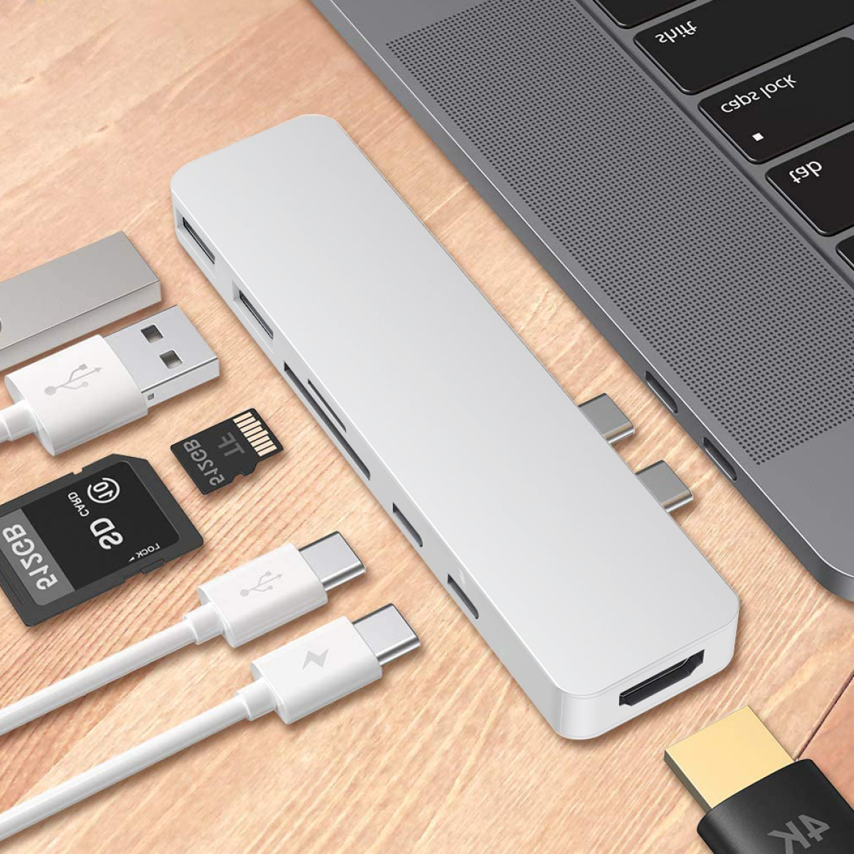 Ein silberner USB-Hub mit mehreren Anschlüssen, an einen Laptop angeschlossen. Weiteres Zubehör wie Karten und Kabel vorhanden.