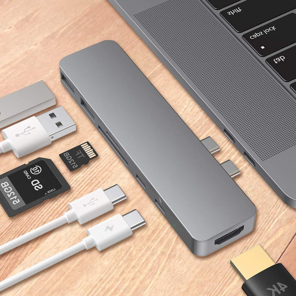 Silberner Hub mit mehreren USB-Anschlüssen, SD-Karte und USB-C-Kabeln. Ein Laptop ist in der Nähe.