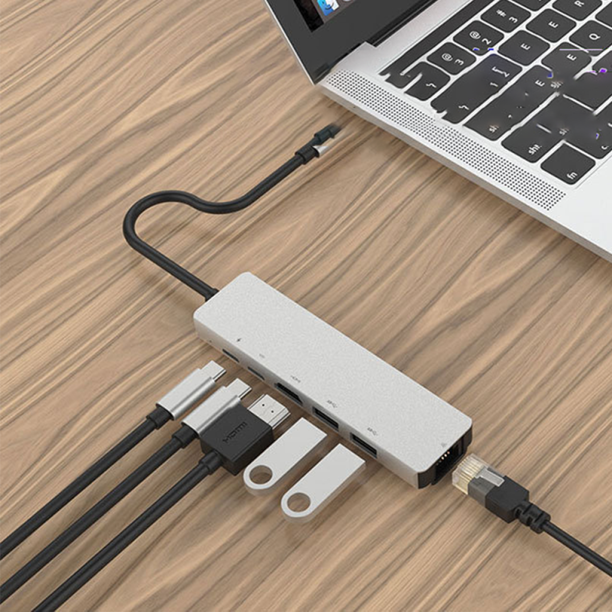 Ein Laptop ist mit einem silbernen Hub verbunden, an dem mehrere Kabel und USB-Laufwerke angeschlossen sind. Der Hub steht auf Holz.