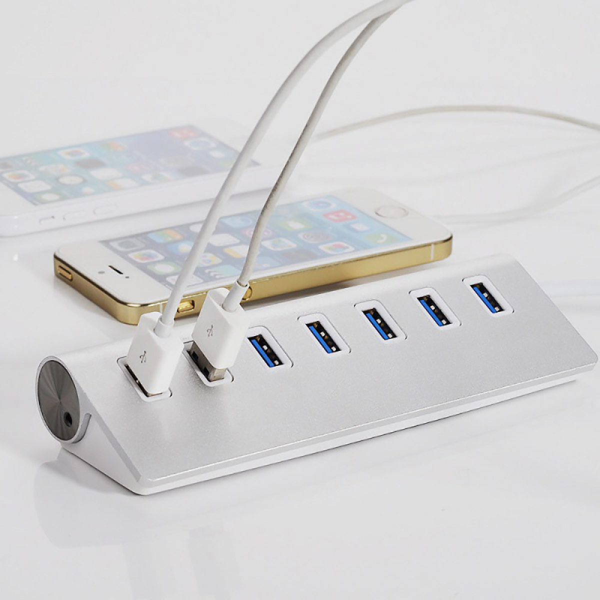 Ein silberner USB-Hub mit mehreren USB-Anschlüssen und zwei daran angeschlossenen Handys auf weißem Grund.